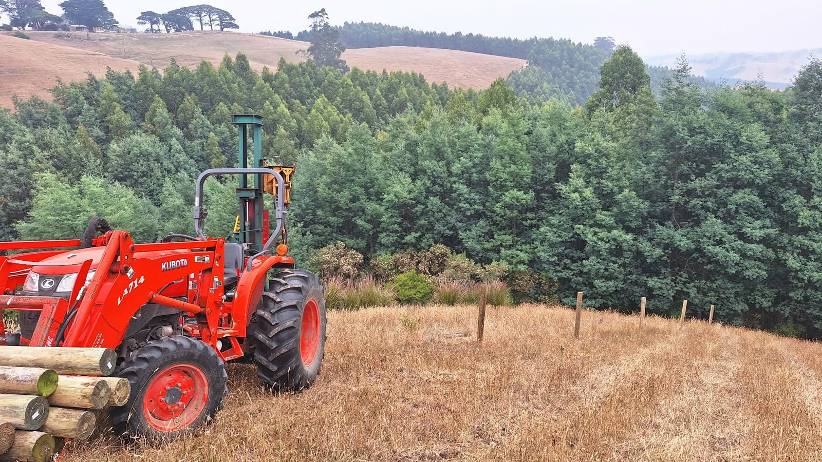 Tractor and post driver with fence posts loaded, overlooking a pine plantation