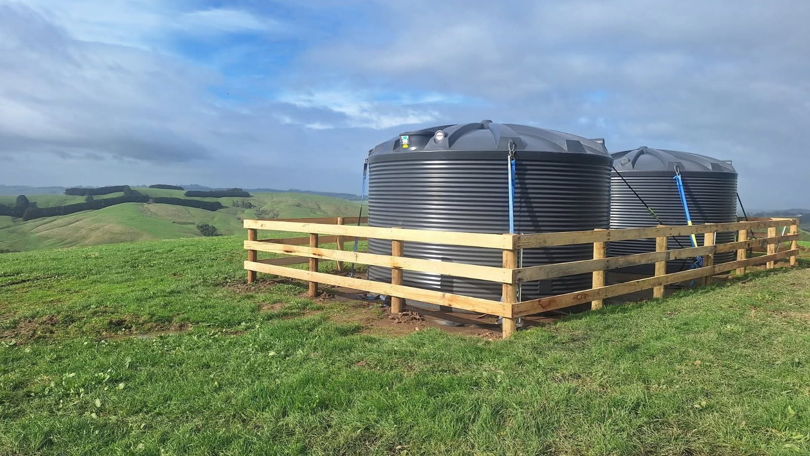 Twin rainwater tanks in a new timber-rail enclosure overlooking the hills