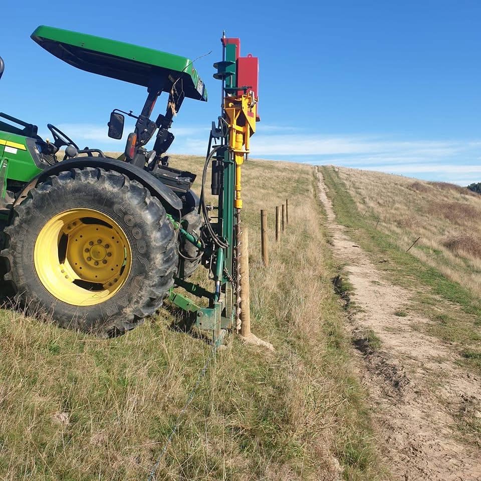Tractor drilling fence posts in rural paddock
